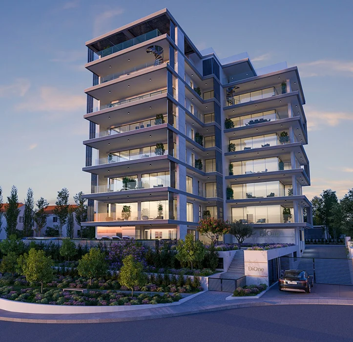 A modern multi-story apartment building with large glass windows and balconies, surrounded by landscaped gardens and a parked car at the entrance, under a clear evening sky.