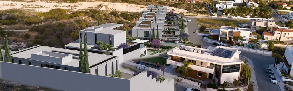 A modern hillside residential neighborhood with contemporary homes, green landscaping, and solar panels, overlooking a coastal town and the sea in the background.